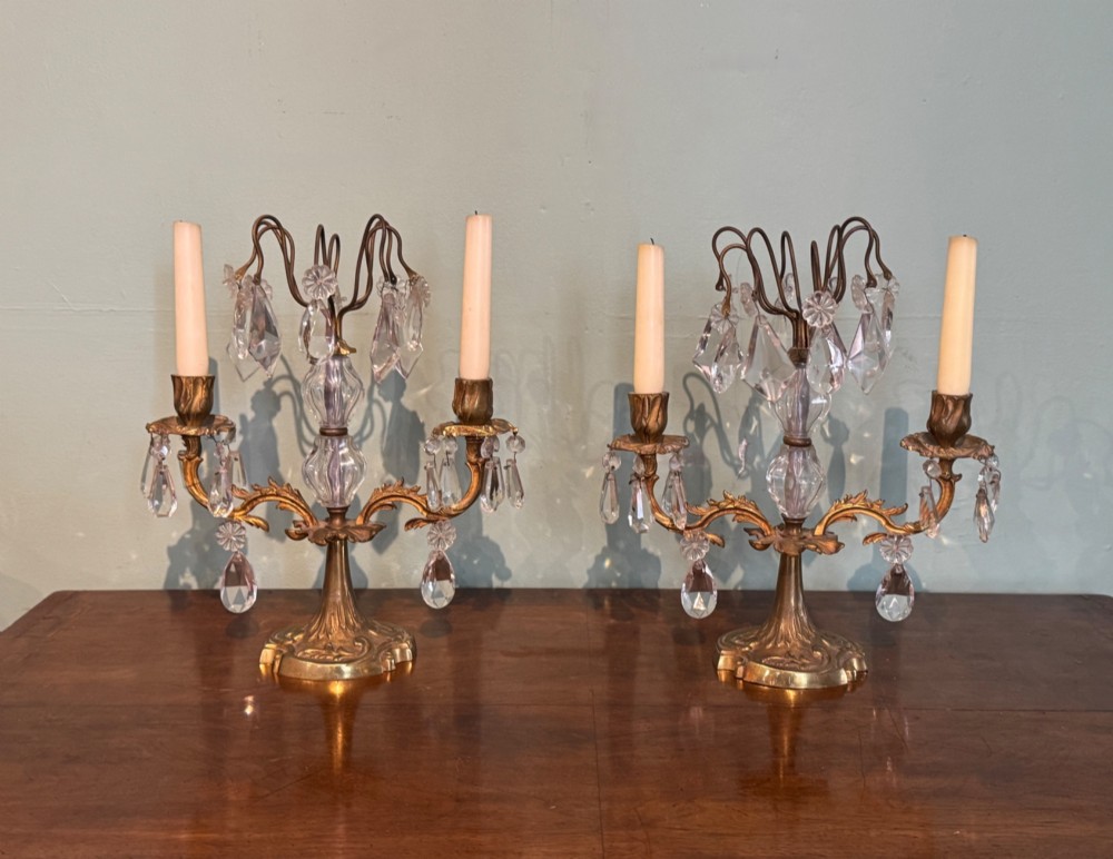 A pair of French gilt-brass two-arm candlestick lustres featuring central crystal elements and hanging cut-crystal drop prisms.