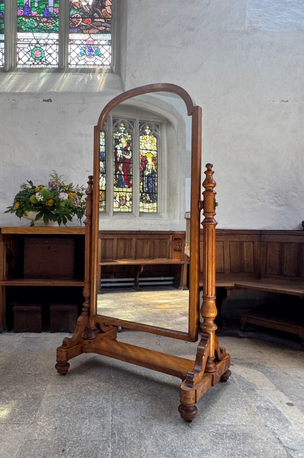 A Victorian satin birch freestanding cheval mirror featuring an arched frame supported by turned side columns and a sturdy trestle base.