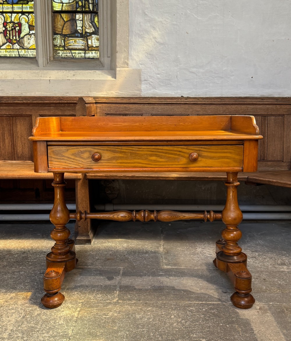 A Victorian pitch pine washstand featuring a raised gallery splashback, a single wide drawer with wooden knobs, and turned trestle legs connected by a stretcher. View V