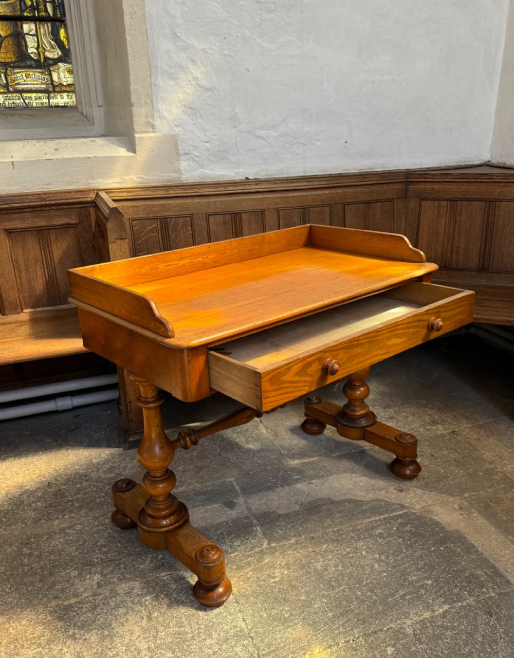 A Victorian pitch pine washstand featuring a raised gallery splashback, a single wide drawer with wooden knobs, and turned trestle legs connected by a stretcher. View VI