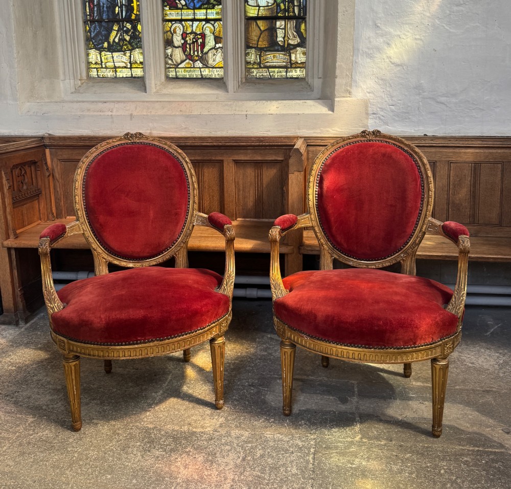 A pair of 19th-century Louis XVI style giltwood armchairs featuring crimson red velvet upholstery and carved medallion backs.