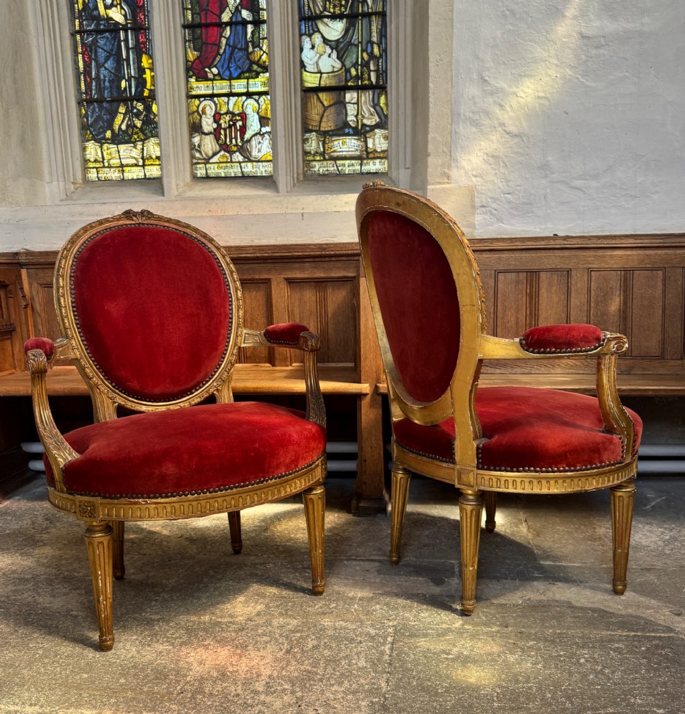 A pair of 19th-century Louis XVI style giltwood armchairs featuring crimson red velvet upholstery and carved medallion backs. View VI