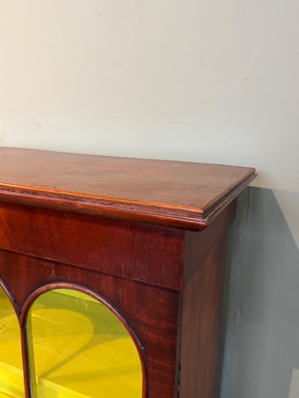 A Victorian dark mahogany two-door cabinet featuring glass doors with arched glazing bars and a bright yellow painted interior with shelves. View V