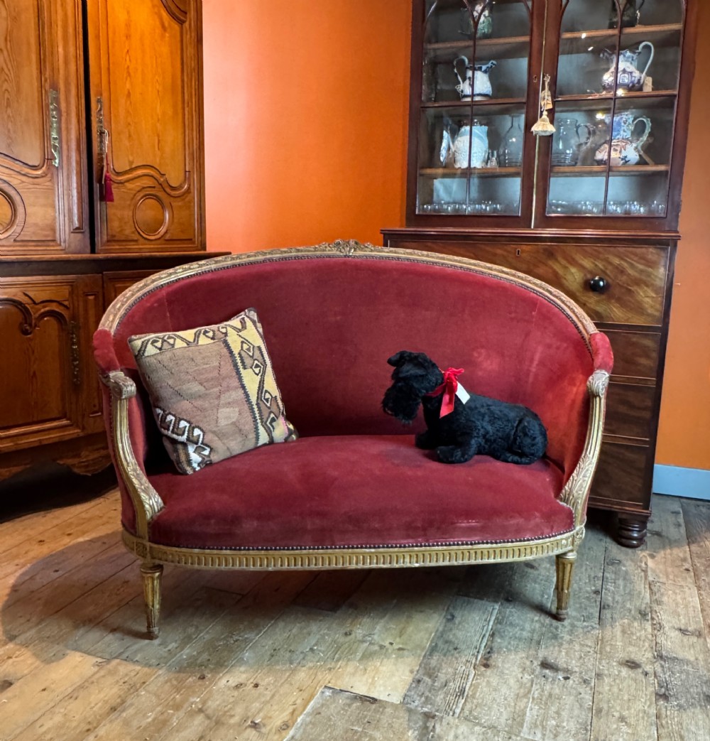 An antique French Louis XVI style two-seat corbeille sofa featuring a carved giltwood frame and deep crimson red velvet upholstery. View II