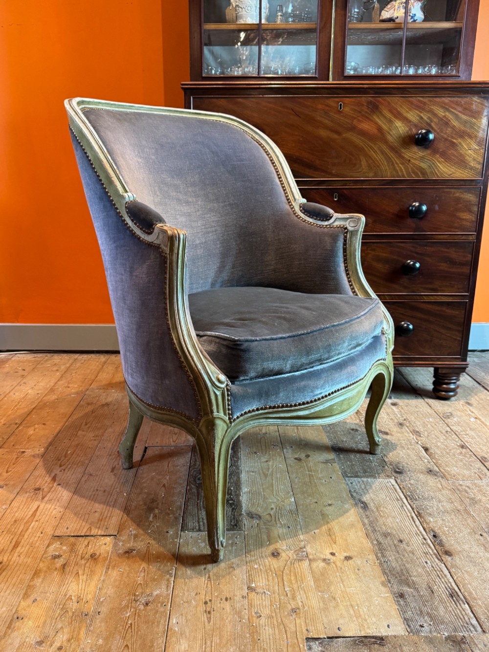 An antique Louis XV style tub bergere armchair upholstered in slate grey velvet with a carved distressed green wooden frame and cabriole legs. View II