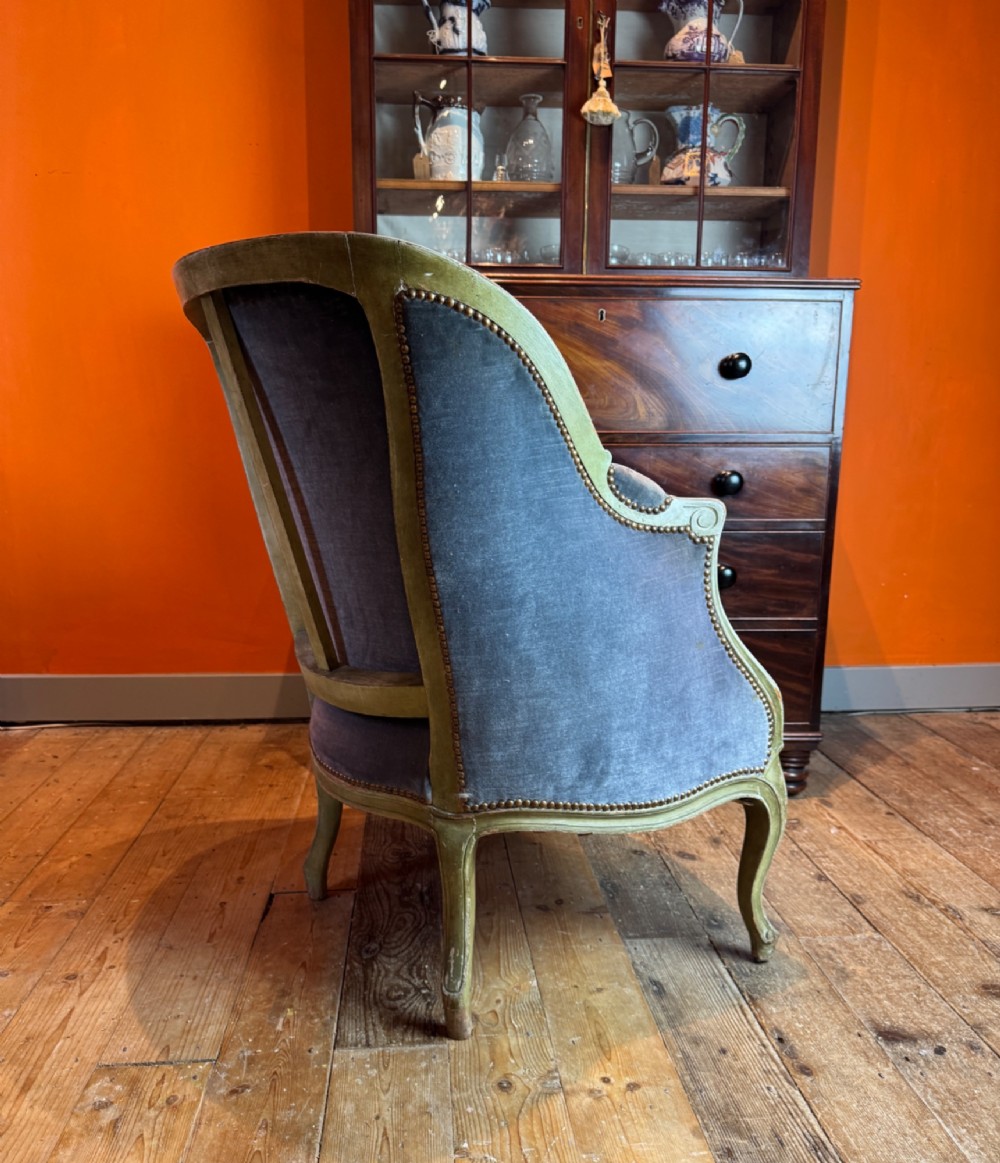 An antique Louis XV style tub bergere armchair upholstered in slate grey velvet with a carved distressed green wooden frame and cabriole legs. View V