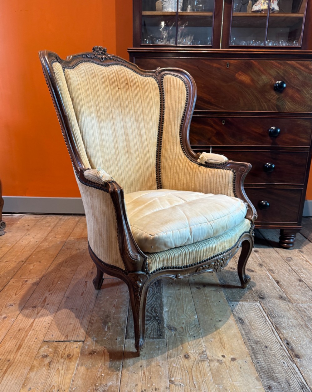 A Louis XV style bergere armchair featuring a carved dark wooden frame, enclosed upholstered arms, beige fabric, and cabriole legs.