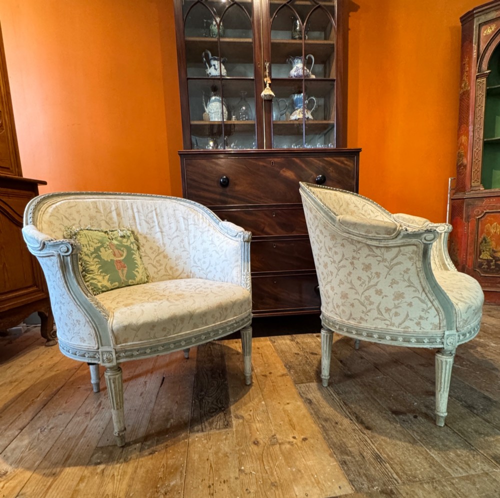 A pair of French tub armchairs featuring distressed cream painted carved wooden frames and light floral upholstery.