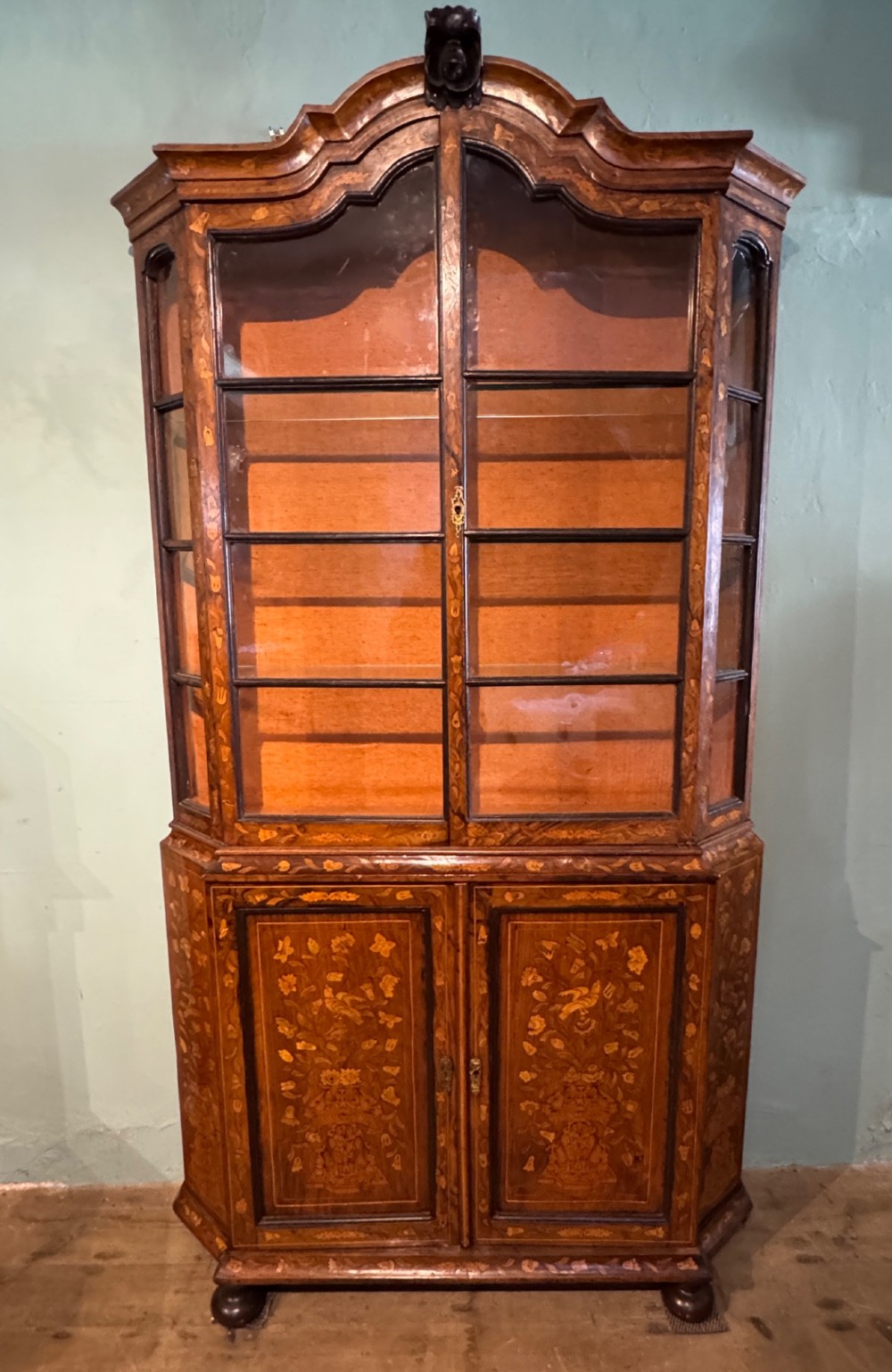 An antique Dutch walnut display cabinet featuring intricate floral marquetry inlays, glazed upper doors, and a double cupboard lower section supported by bun feet.