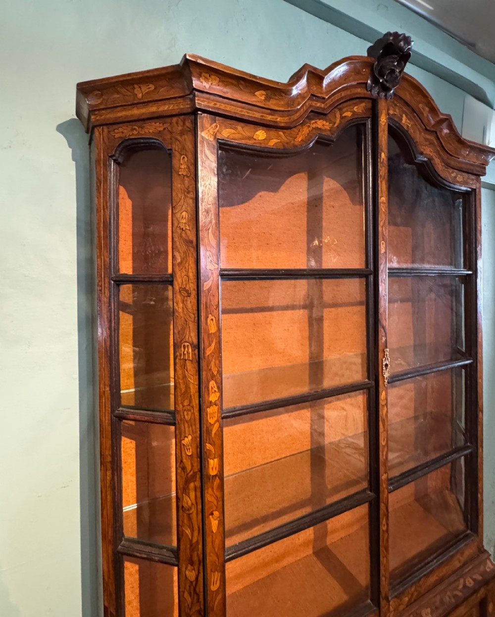 An antique Dutch walnut display cabinet featuring intricate floral marquetry inlays, glazed upper doors, and a double cupboard lower section supported by bun feet. View III