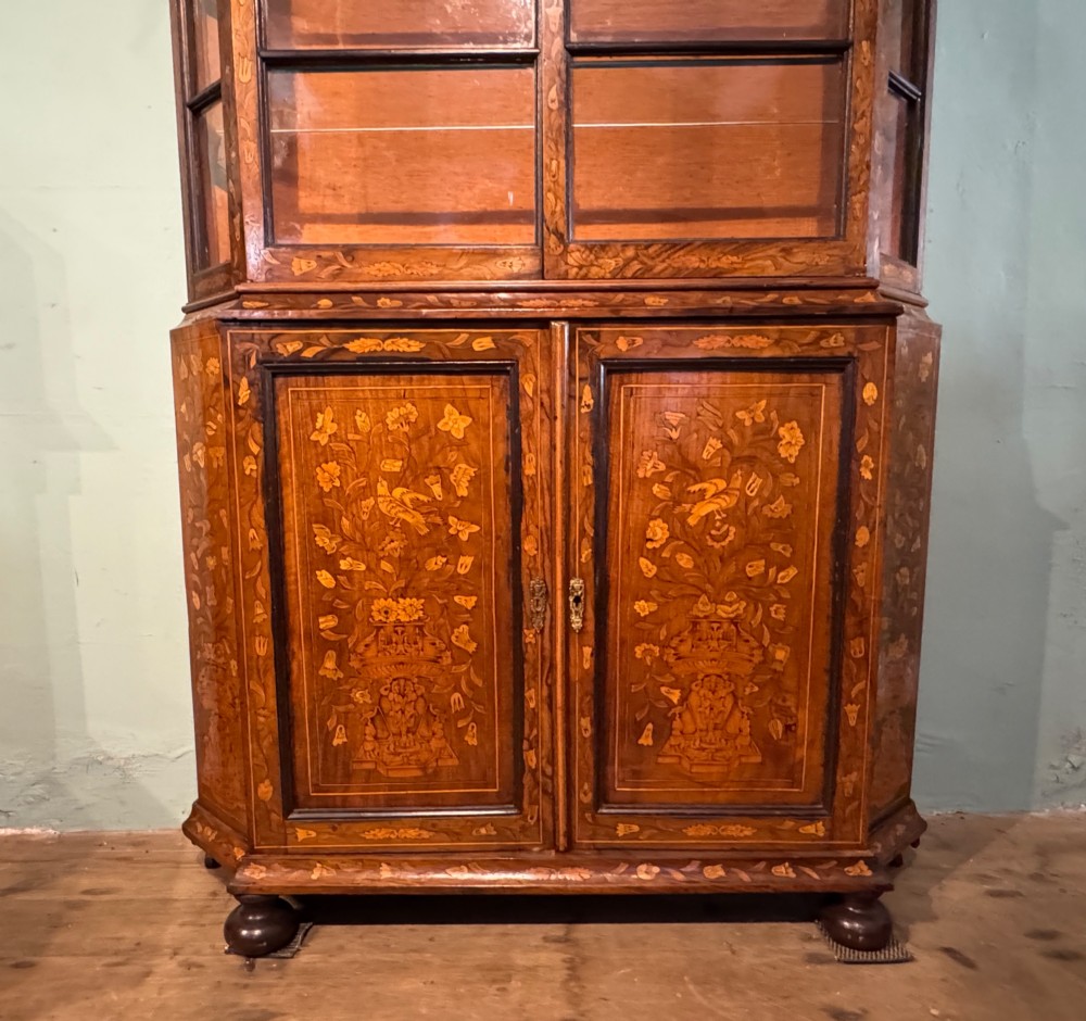 An antique Dutch walnut display cabinet featuring intricate floral marquetry inlays, glazed upper doors, and a double cupboard lower section supported by bun feet. View IV