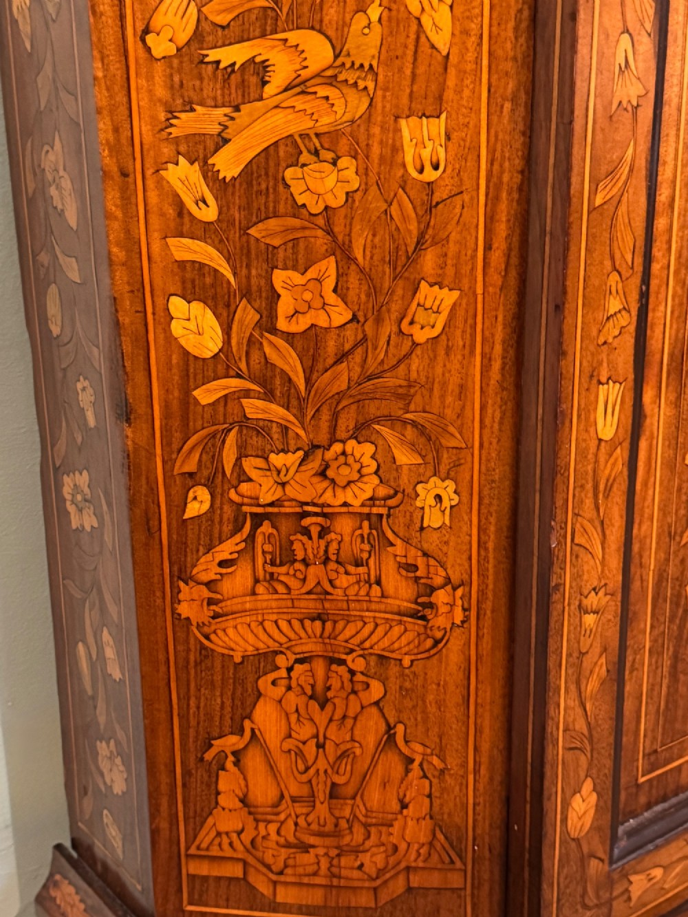 An antique Dutch walnut display cabinet featuring intricate floral marquetry inlays, glazed upper doors, and a double cupboard lower section supported by bun feet. View VI