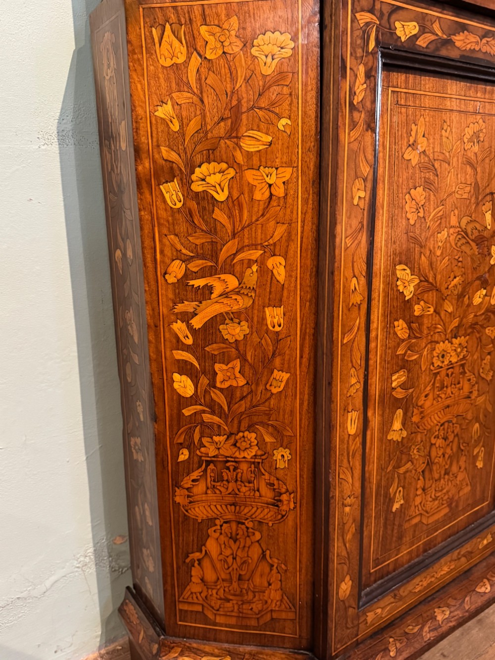 An antique Dutch walnut display cabinet featuring intricate floral marquetry inlays, glazed upper doors, and a double cupboard lower section supported by bun feet. View VII