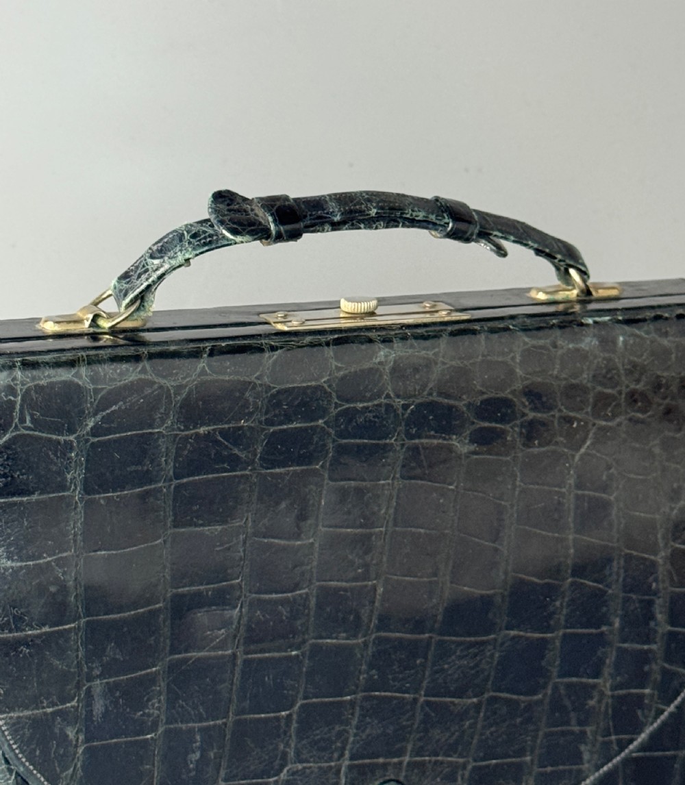A black crocodile leather rectangular vanity case featuring a curved front flap pocket, top handle, and brass clasp. View II