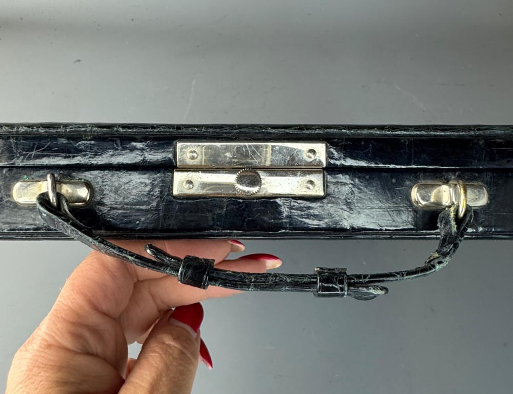 A black crocodile leather rectangular vanity case featuring a curved front flap pocket, top handle, and brass clasp. View IV