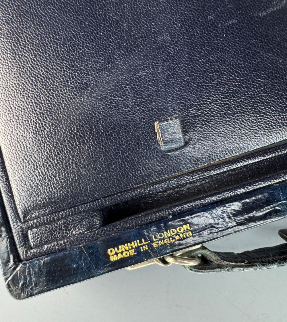 A black crocodile leather rectangular vanity case featuring a curved front flap pocket, top handle, and brass clasp. View VII