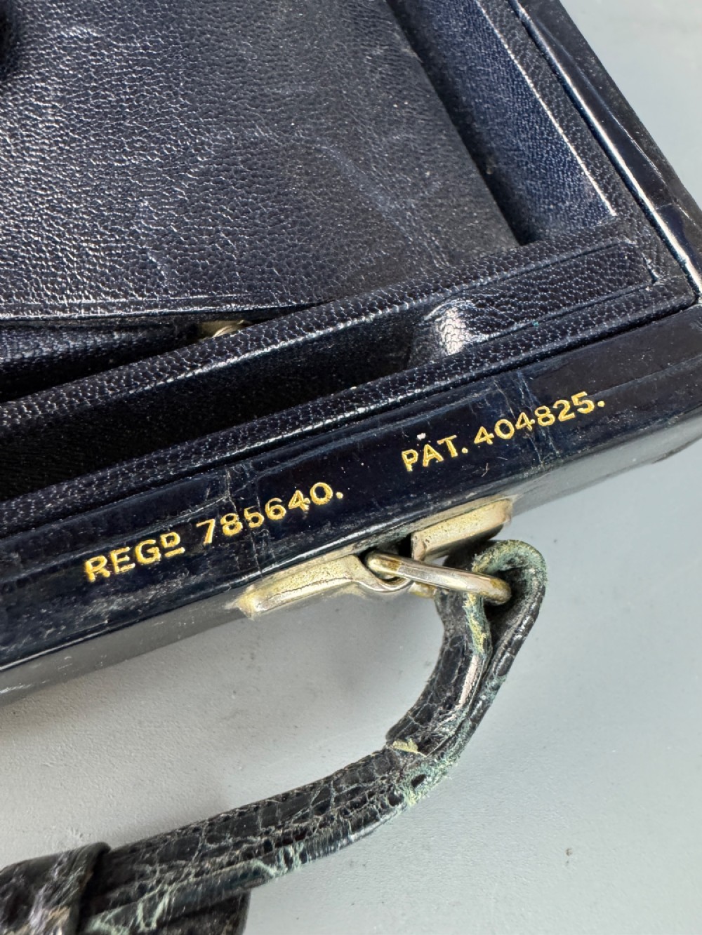 A black crocodile leather rectangular vanity case featuring a curved front flap pocket, top handle, and brass clasp. View XIII