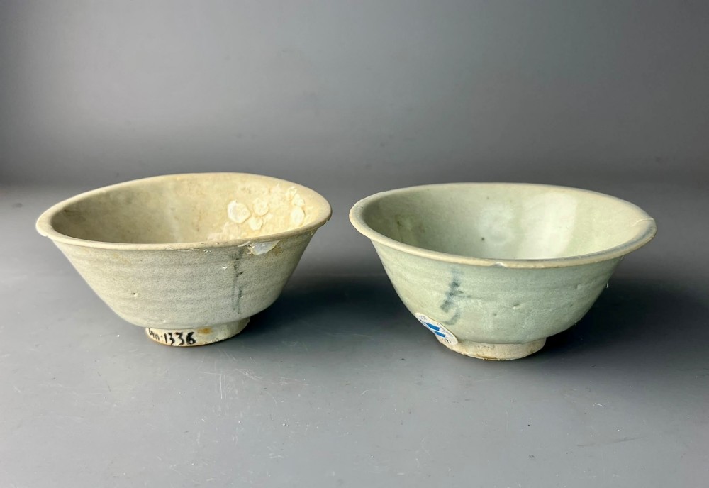A pair of small antique Chinese porcelain bowls with flared rims, raised foot rings, and pale greenish-white glazed finishes displaying subtle surface accretions.