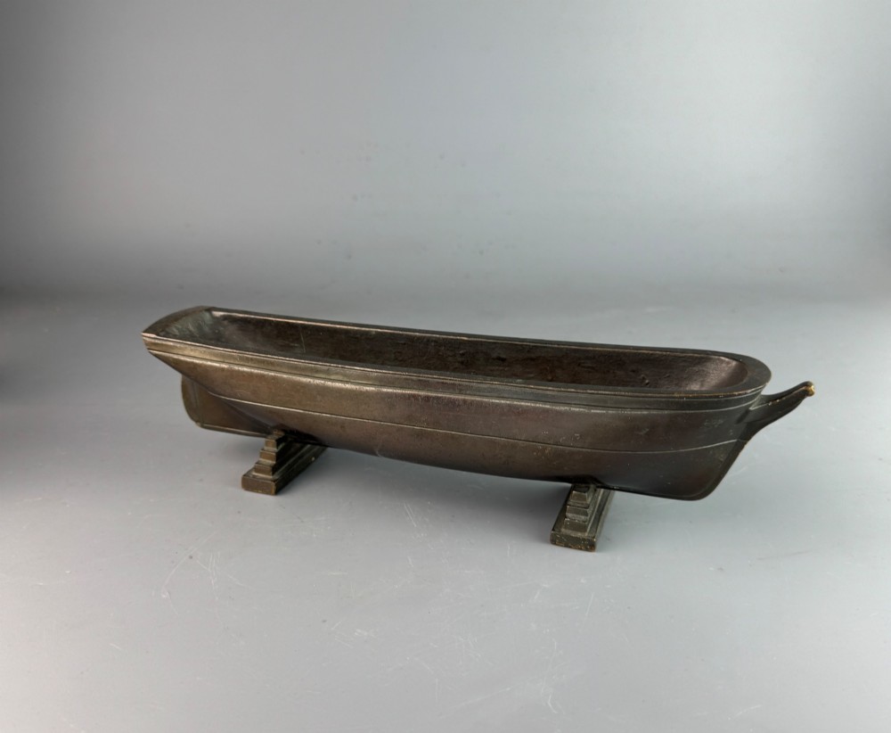 An Art Deco dark bronze pen tray designed in the form of a boat hull mounted on two stepped support feet.