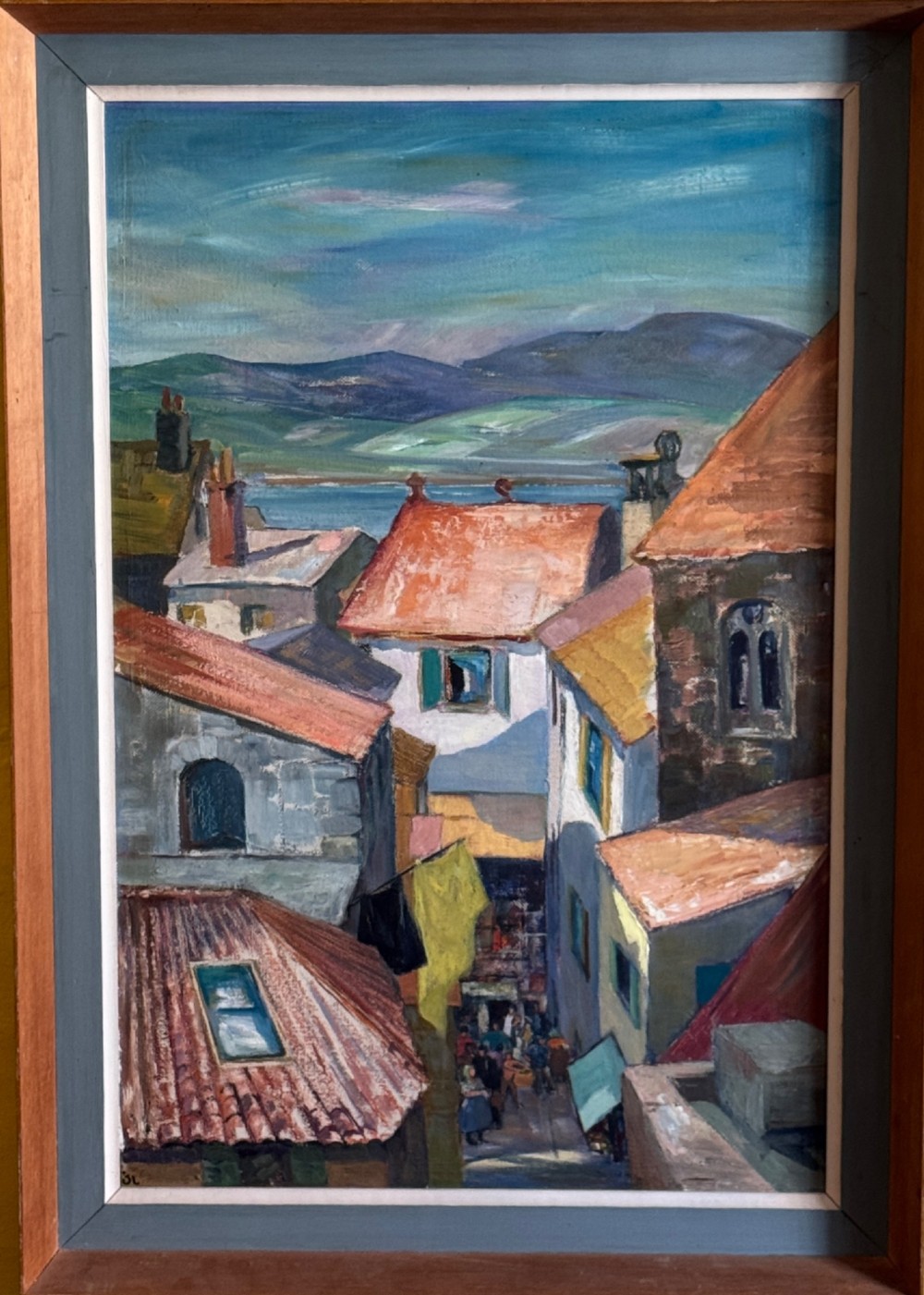 A mid-century oil painting on board depicting a narrow street in Antibes with terracotta roofs and distant mountains, housed in a grey and timber wooden frame. View V