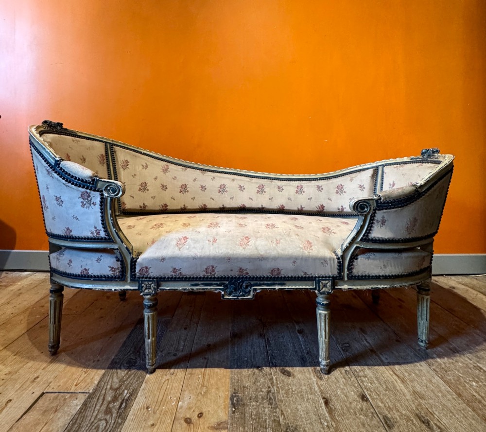 An antique French Louis XVI style duchesse brisee chaise with a distressed off-white painted wooden frame, fluted legs, and floral upholstery. View VI