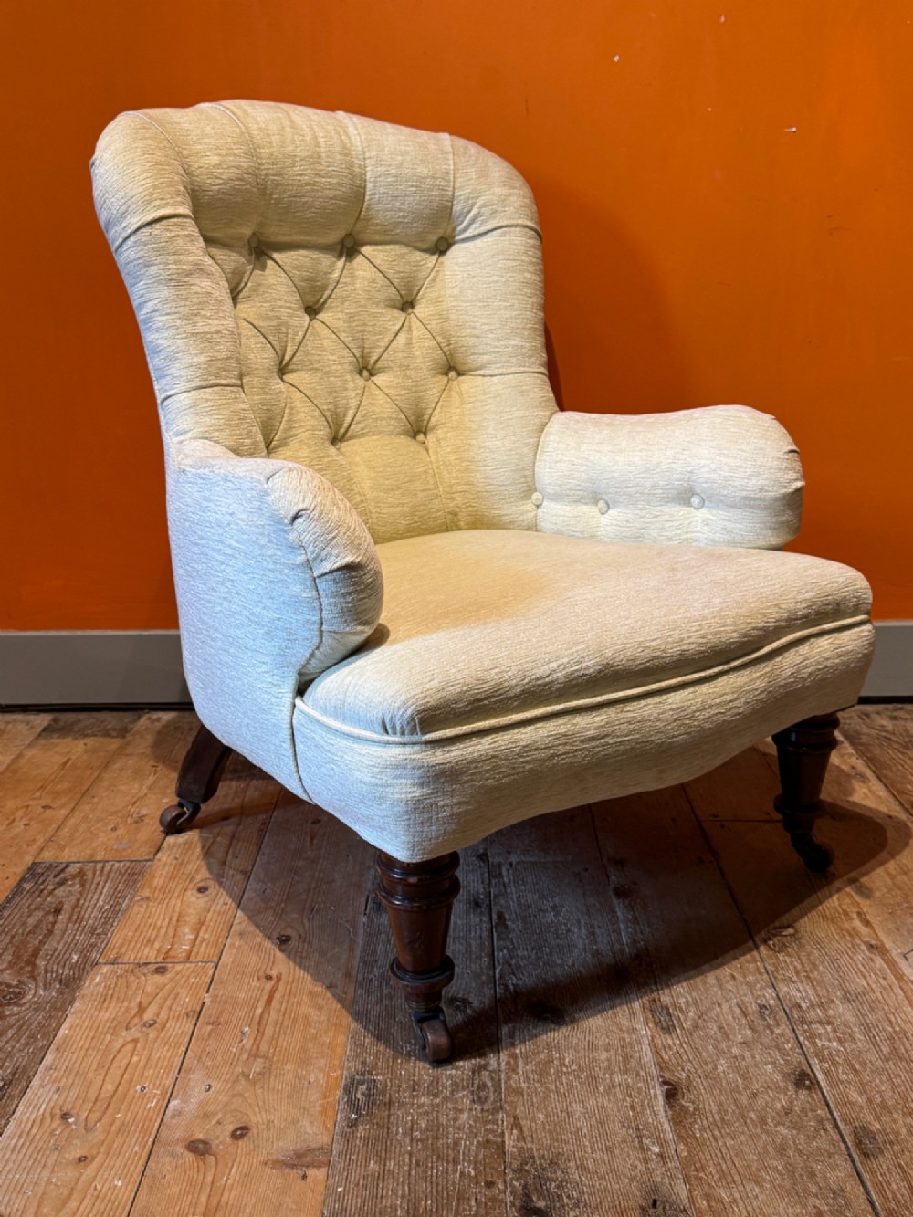 A Victorian armchair upholstered in cream fabric featuring deep button tufting on the backrest, padded arms, and dark turned wooden legs with brass castors. View II