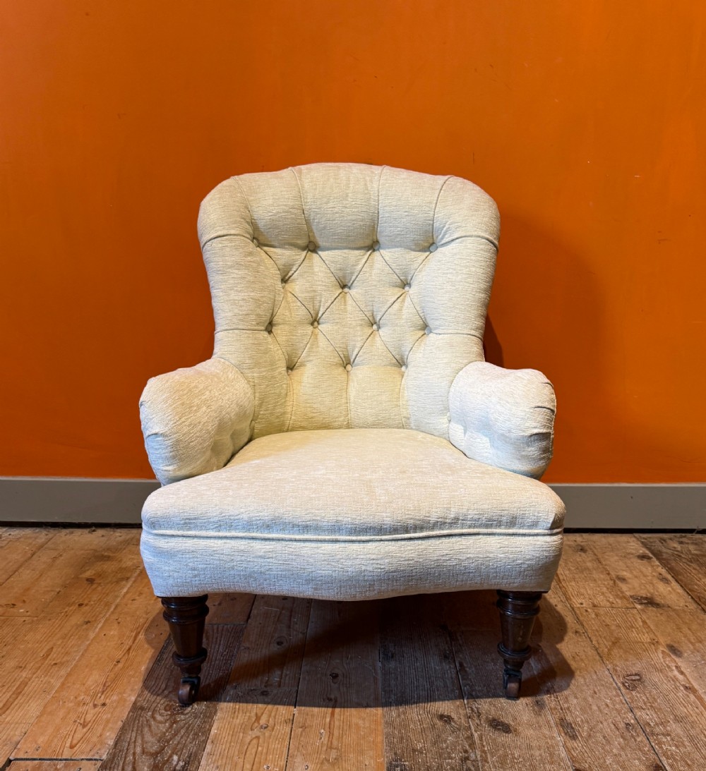 A Victorian armchair upholstered in cream fabric featuring deep button tufting on the backrest, padded arms, and dark turned wooden legs with brass castors. View III