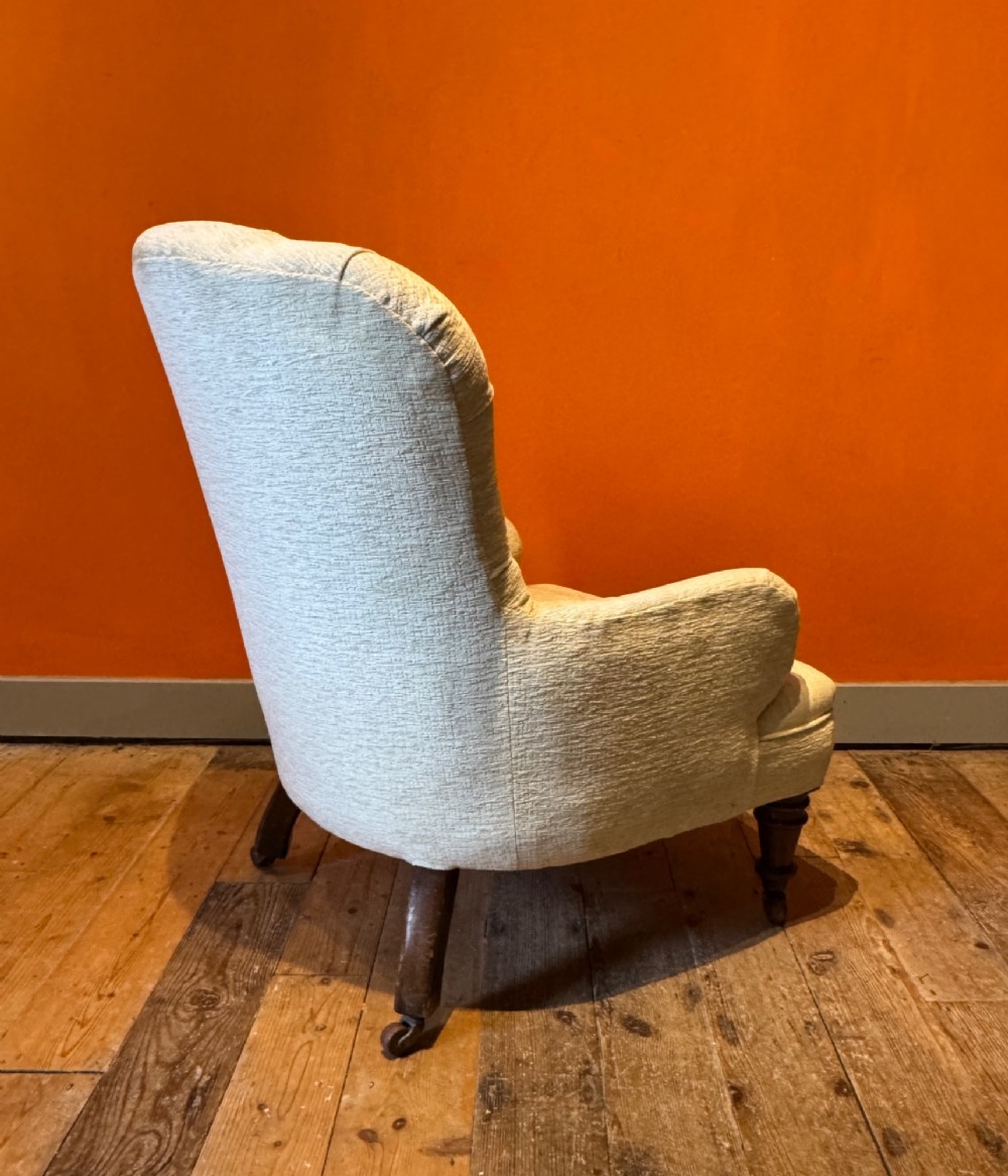 A Victorian armchair upholstered in cream fabric featuring deep button tufting on the backrest, padded arms, and dark turned wooden legs with brass castors. View IV
