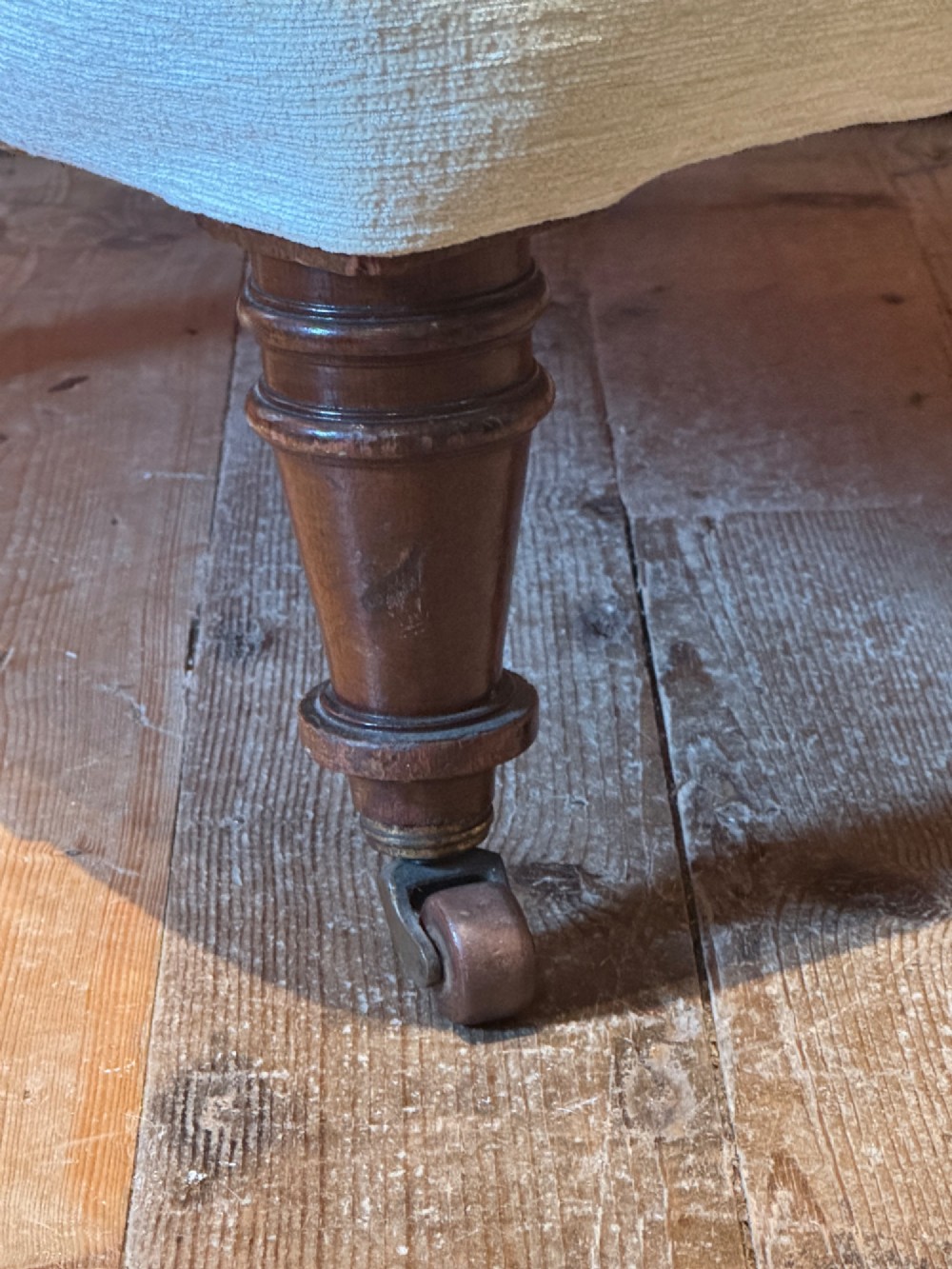 A Victorian armchair upholstered in cream fabric featuring deep button tufting on the backrest, padded arms, and dark turned wooden legs with brass castors. View VI