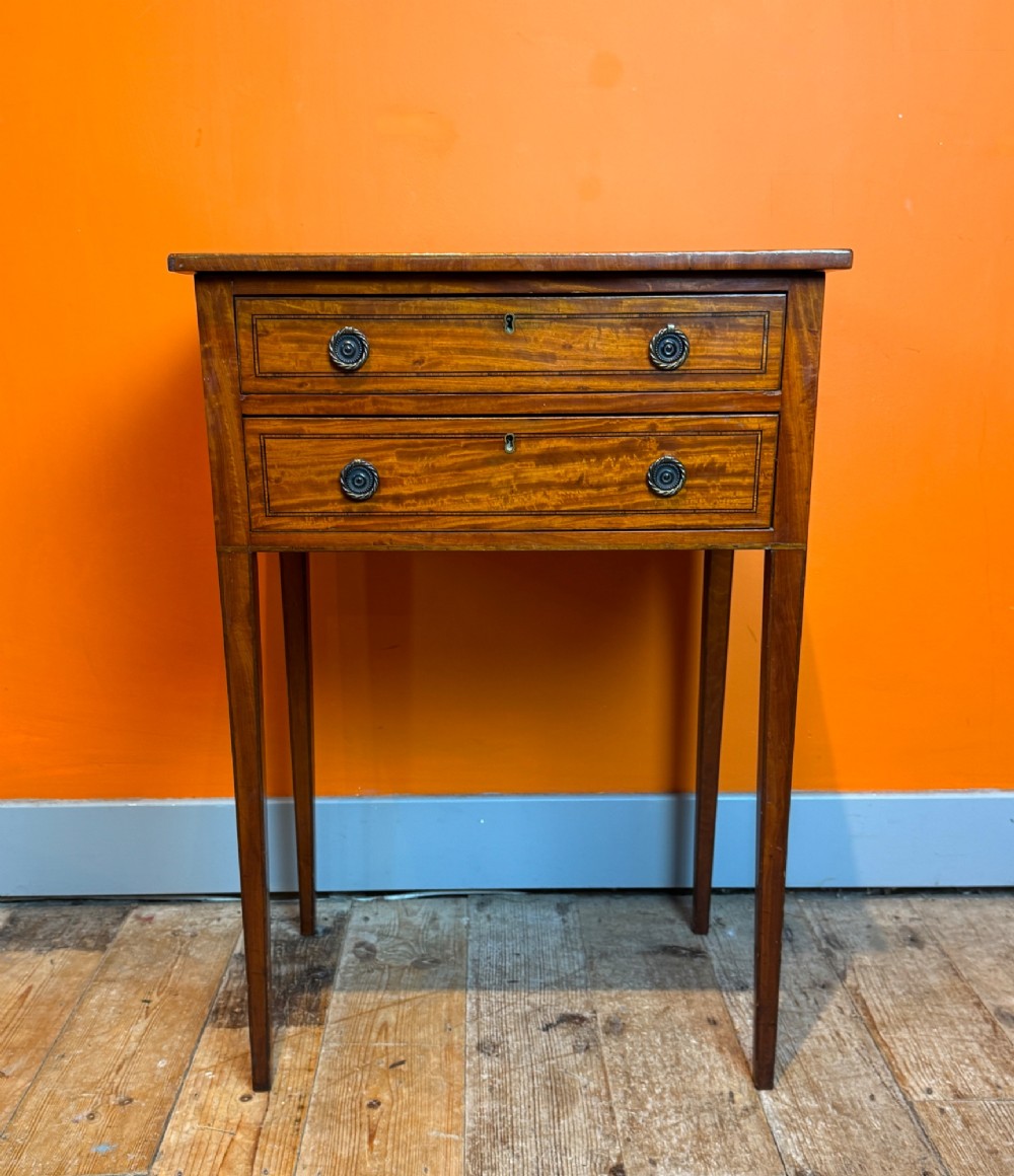 A Sheraton style satinwood side table featuring two crossbanded drawers with round brass pulls and square tapered legs. View II
