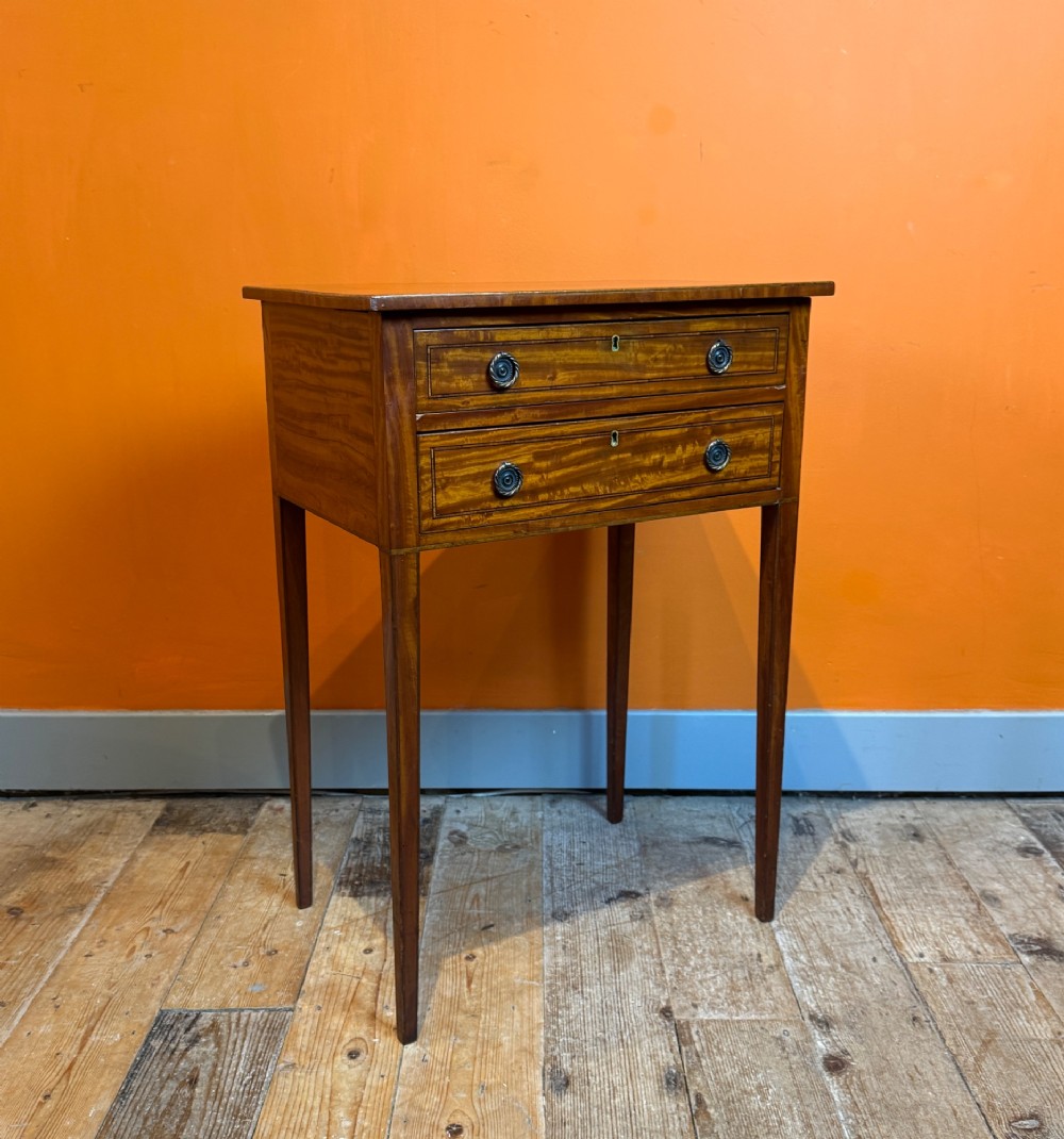 A Sheraton style satinwood side table featuring two crossbanded drawers with round brass pulls and square tapered legs. View V