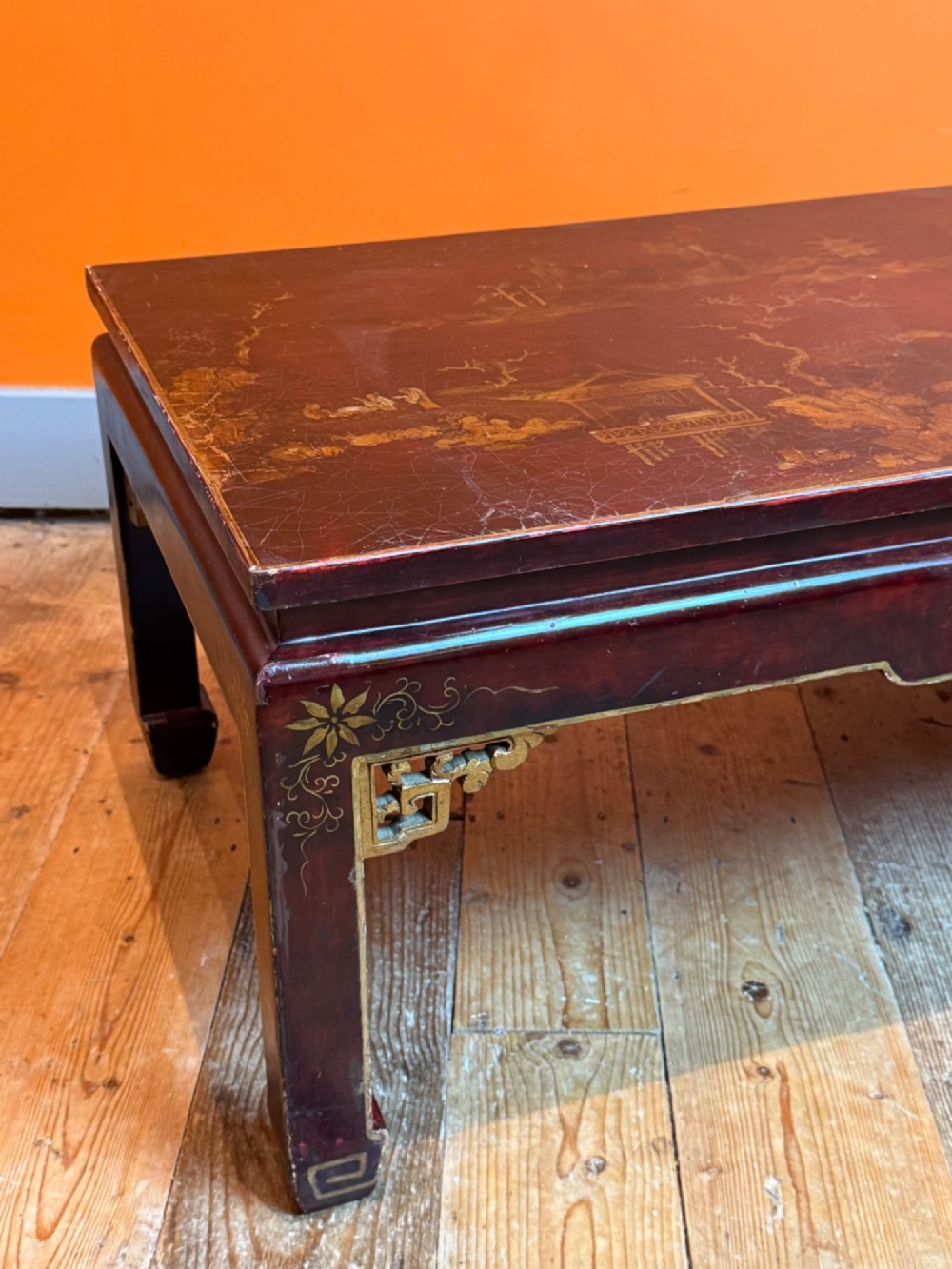 A low rectangular coffee table with a dark red lacquer finish featuring gilded hand-painted Asian landscape scenes and decorated corner spandrels. View II