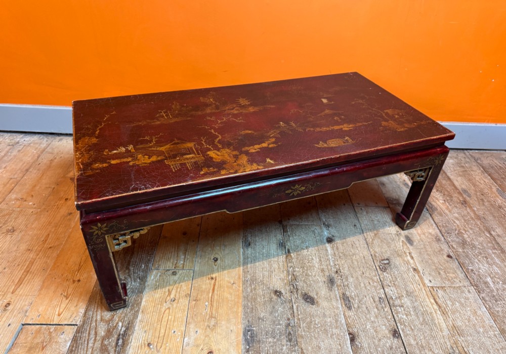 A low rectangular coffee table with a dark red lacquer finish featuring gilded hand-painted Asian landscape scenes and decorated corner spandrels. View III