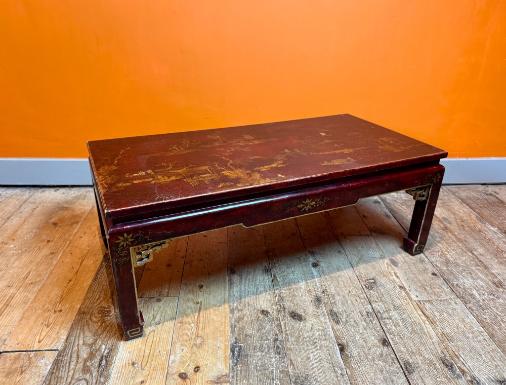 A low rectangular coffee table with a dark red lacquer finish featuring gilded hand-painted Asian landscape scenes and decorated corner spandrels. View IV