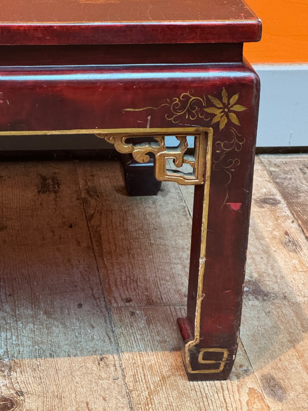 A low rectangular coffee table with a dark red lacquer finish featuring gilded hand-painted Asian landscape scenes and decorated corner spandrels. View V