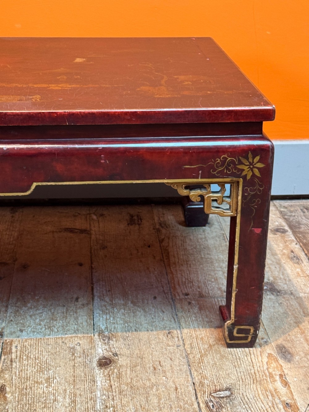 A low rectangular coffee table with a dark red lacquer finish featuring gilded hand-painted Asian landscape scenes and decorated corner spandrels. View VI