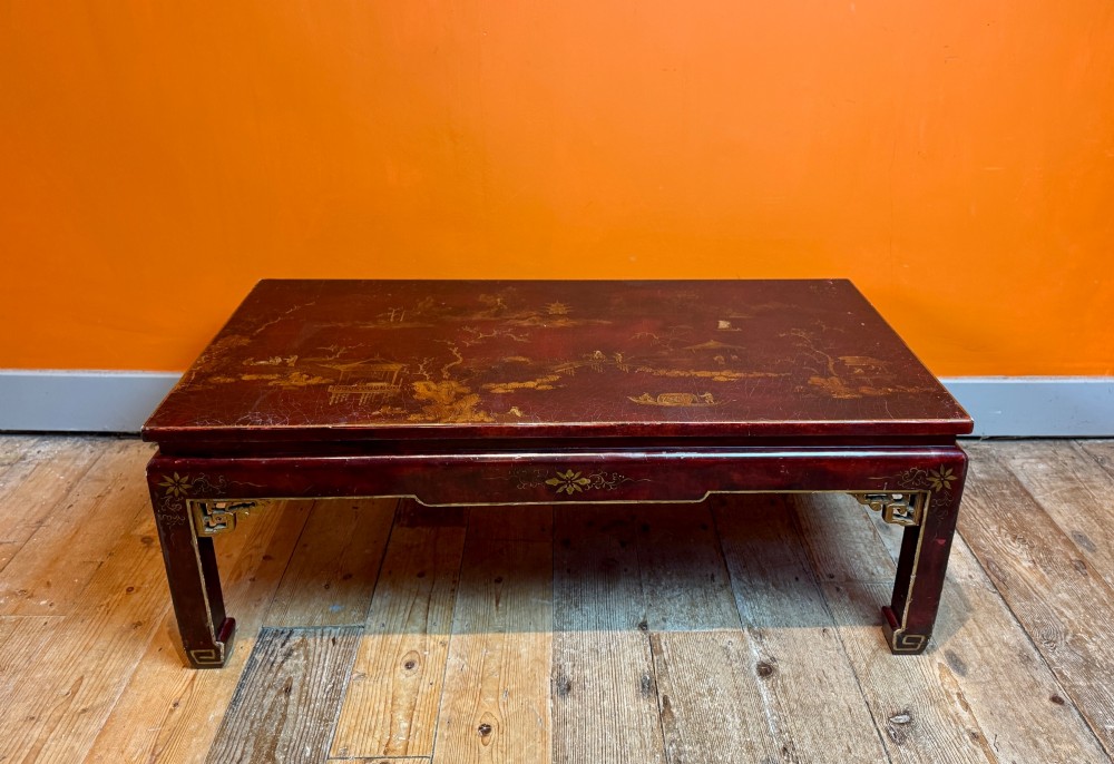 A low rectangular coffee table with a dark red lacquer finish featuring gilded hand-painted Asian landscape scenes and decorated corner spandrels. View VII