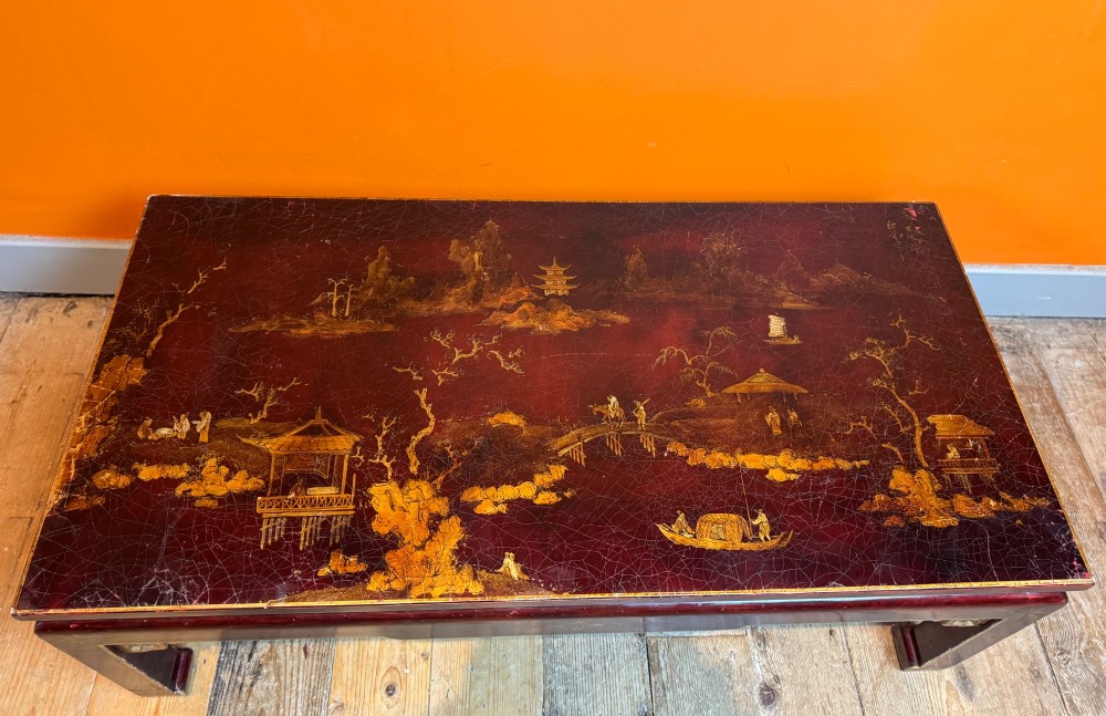 A low rectangular coffee table with a dark red lacquer finish featuring gilded hand-painted Asian landscape scenes and decorated corner spandrels. View VIII