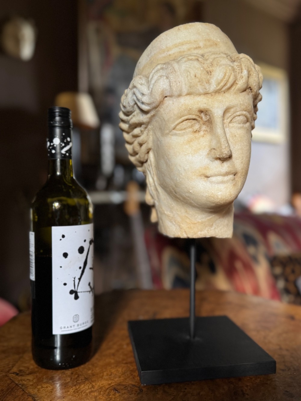 A carved white marble head of a classical goddess wearing a diadem, mounted on a slender dark metal display stand. View III