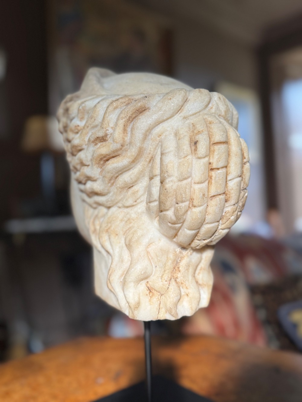 A carved white marble head of a classical goddess wearing a diadem, mounted on a slender dark metal display stand. View V