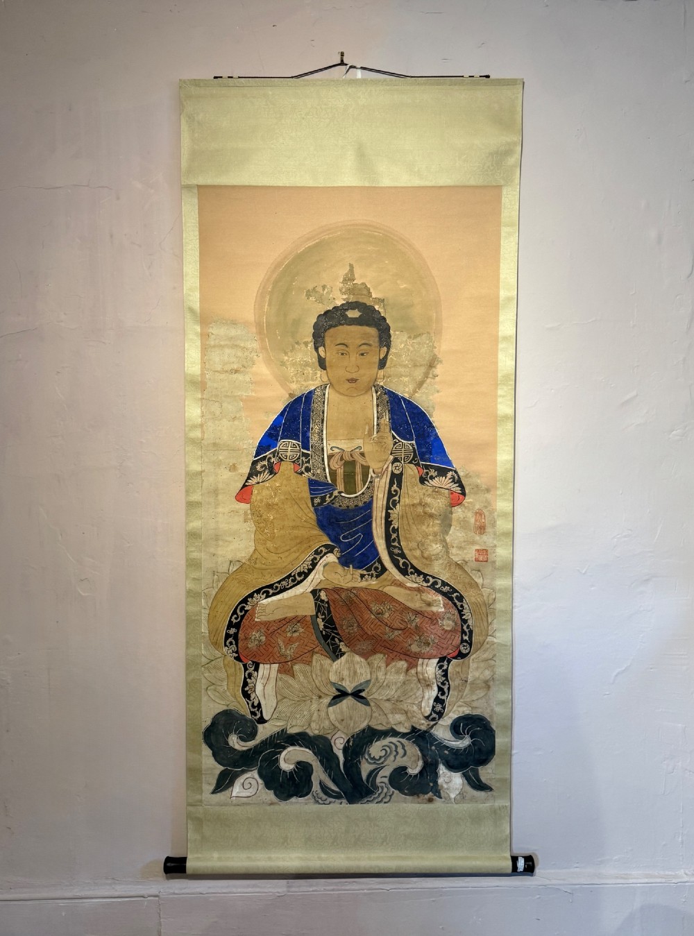 A 19th-century Chinese hanging scroll painting depicting Buddha Shakyamuni seated cross-legged on a lotus throne in blue and gold robes.