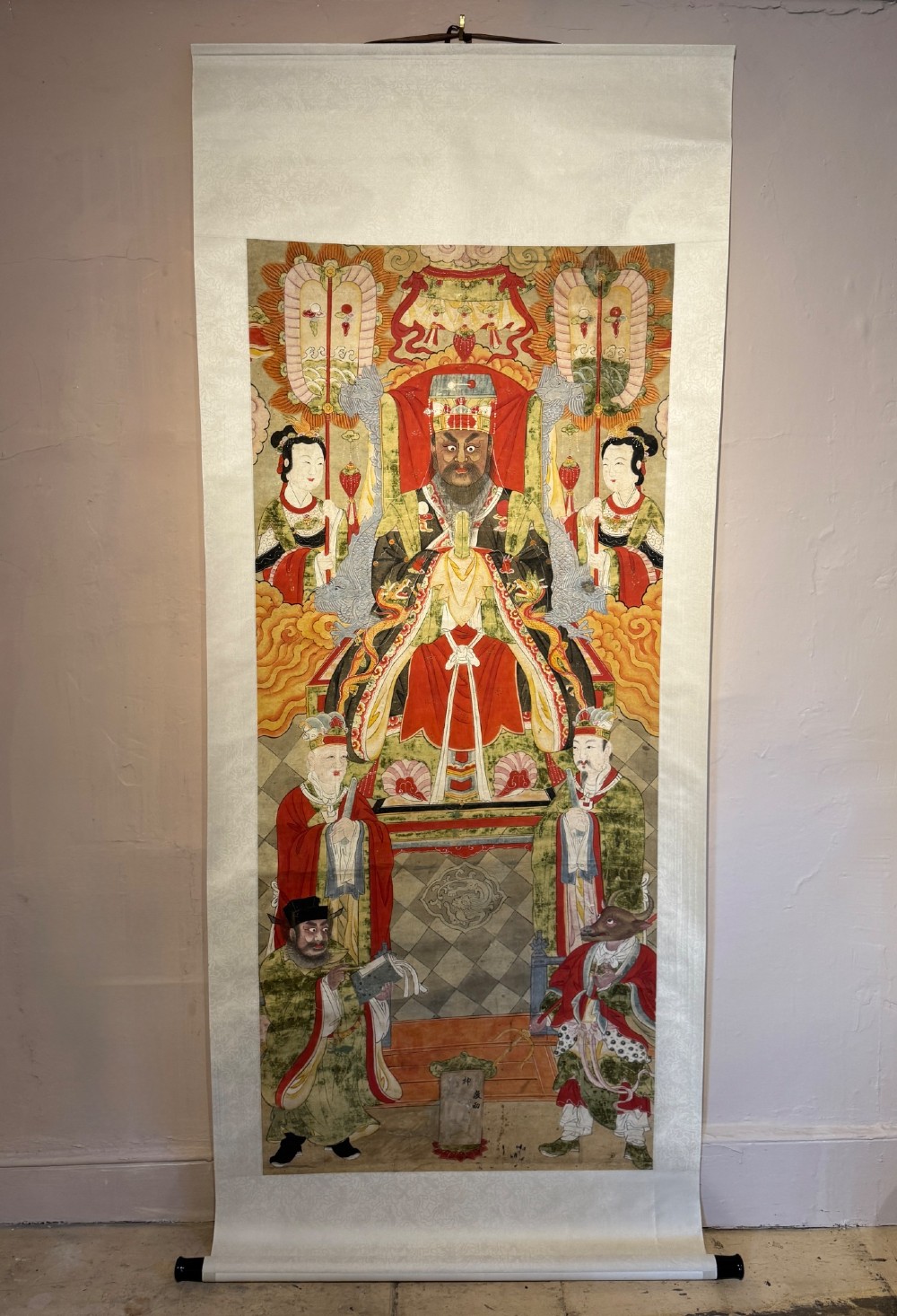 A vertical 19th-century Chinese hanging scroll painting on a pale silk mount depicting an enthroned Daoist judge surrounded by court attendants and mythological figures in red and green ceremonial robes.
