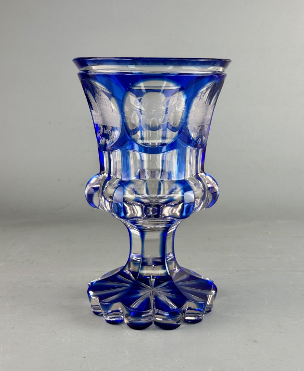 A cobalt blue cut-to-clear glass spa goblet featuring wheel-engraved architectural medallions, a faceted stem, and a starburst base.
