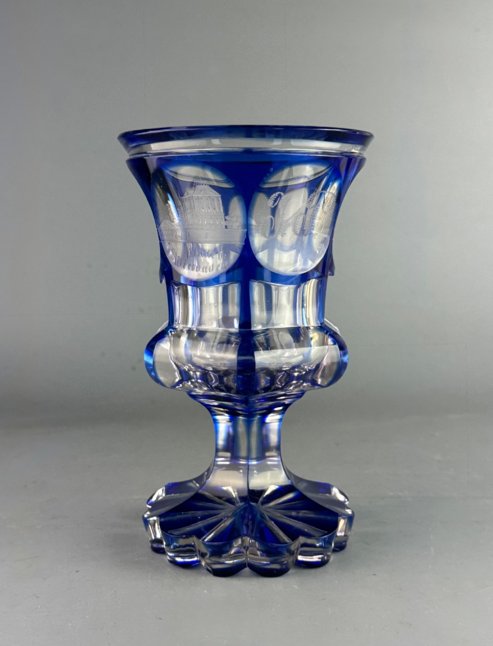 A cobalt blue cut-to-clear glass spa goblet featuring wheel-engraved architectural medallions, a faceted stem, and a starburst base. View II