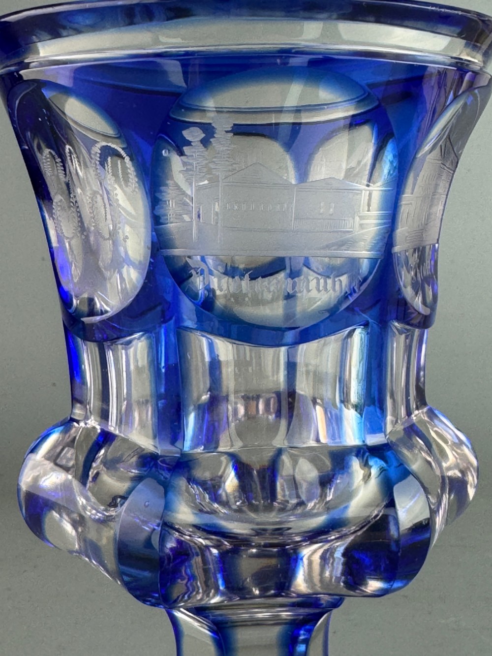 A cobalt blue cut-to-clear glass spa goblet featuring wheel-engraved architectural medallions, a faceted stem, and a starburst base. View V