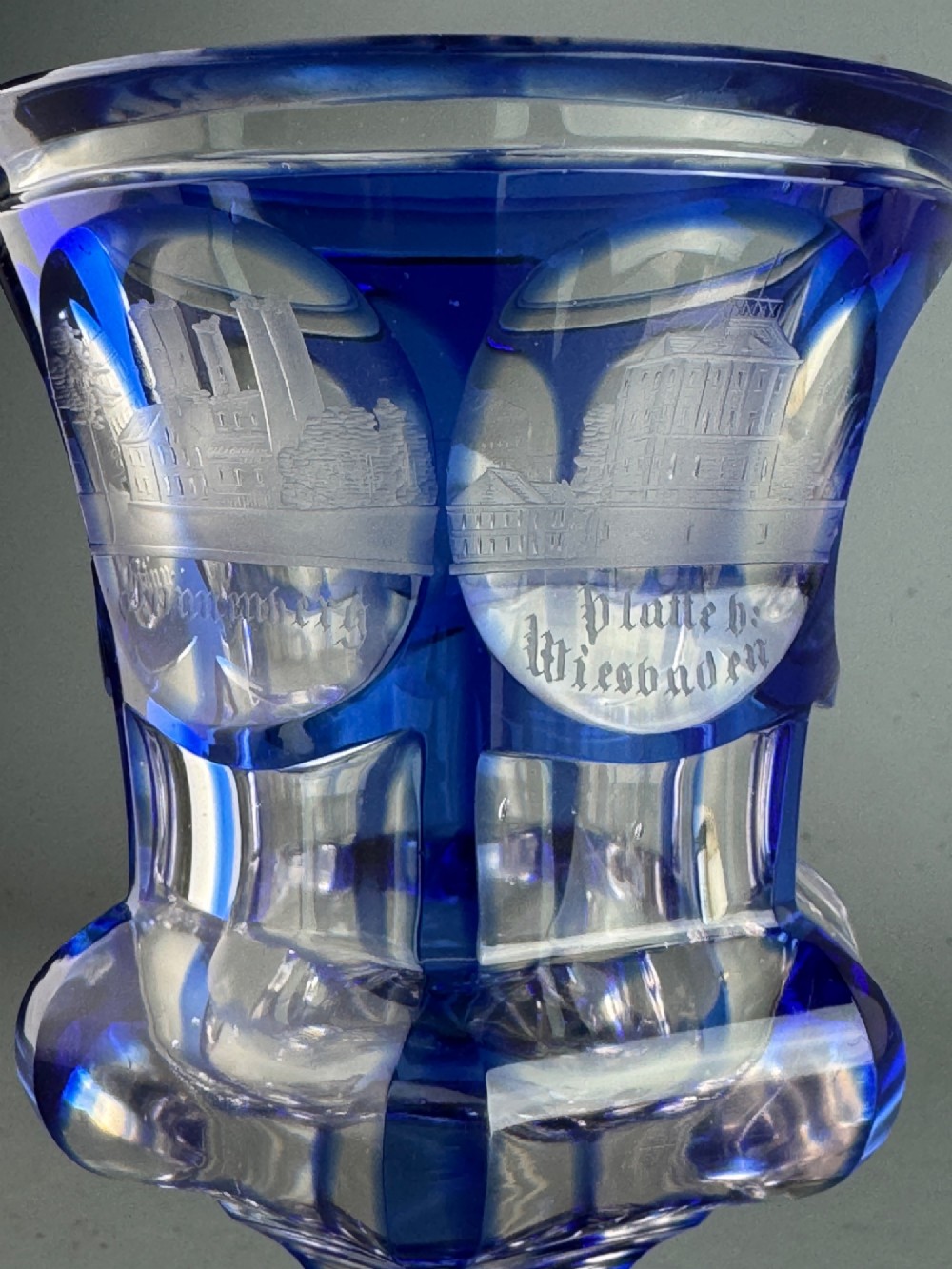 A cobalt blue cut-to-clear glass spa goblet featuring wheel-engraved architectural medallions, a faceted stem, and a starburst base. View VI