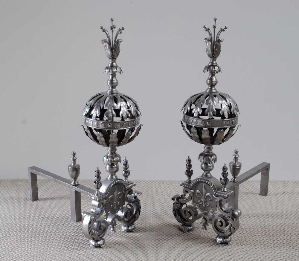 A pair of decorative Arts and Crafts steel andirons featuring pierced leaf-form globes, fleur-de-lis motifs, scrolled bases, and floral finials. View II