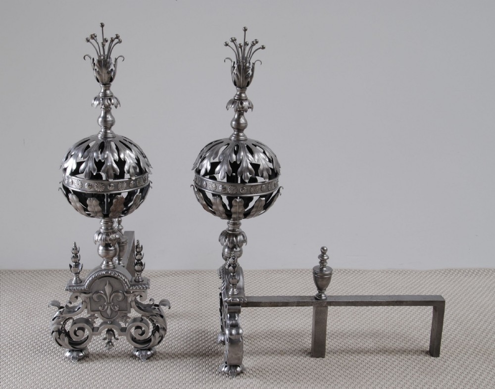 A pair of decorative Arts and Crafts steel andirons featuring pierced leaf-form globes, fleur-de-lis motifs, scrolled bases, and floral finials. View III