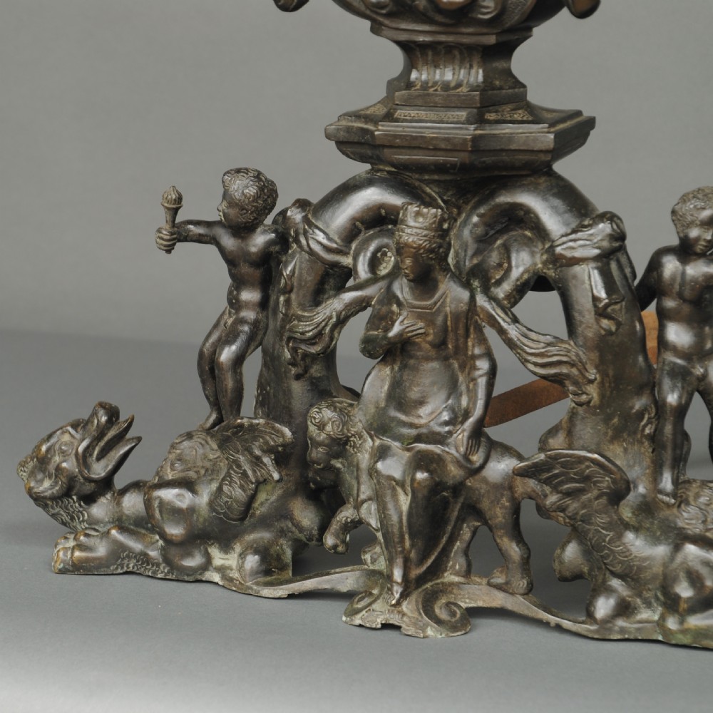 A matching pair of dark patinated bronze 19th-century Italianate andirons featuring standing cherub figures atop elaborate scrollwork and mask bases. View II