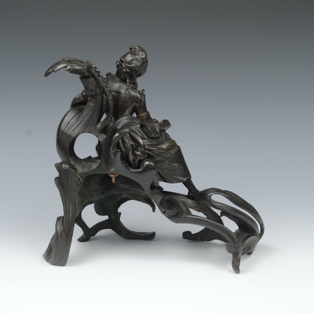 A pair of dark patinated bronze 19th-century French Rococo style chenets featuring sculpted figures seated atop elaborate scrollwork bases. View V